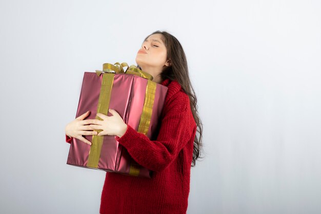 Hermosa mujer joven en suéter rojo de pie y sosteniendo la caja de regalo.