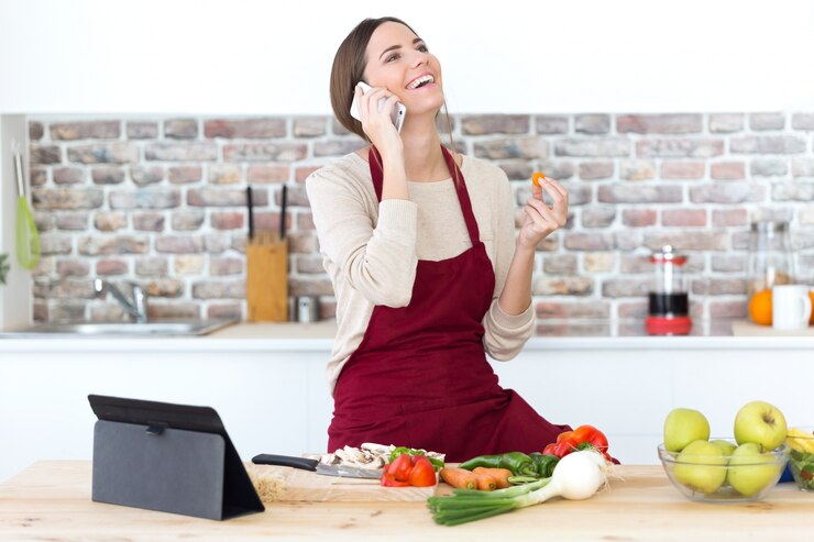 Foto gratuito hermosa mujer joven con teléfono móvil mientras se cocina en la cocina.