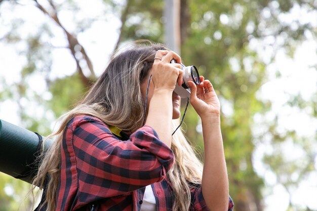 Hermosa mujer joven tomando fotos y senderismo con mochila. Mujer emocionada disparando paisaje y sonriendo. Turismo de mochilero, aventura y concepto de vacaciones de verano.