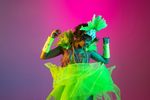 Hermosa mujer joven en traje de carnaval y mascarada sobre fondo de estudio degradado en luz de neón