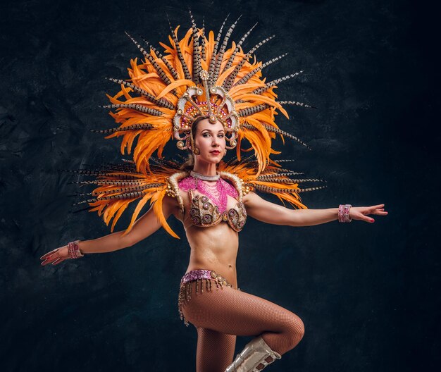 Hermosa mujer joven en traje especial de plumas está bailando en el estudio.