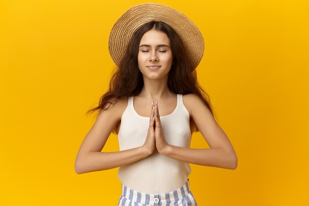 Hermosa mujer joven tranquila agradecida tomados de la mano juntos en namaste y manteniendo los ojos cerrados