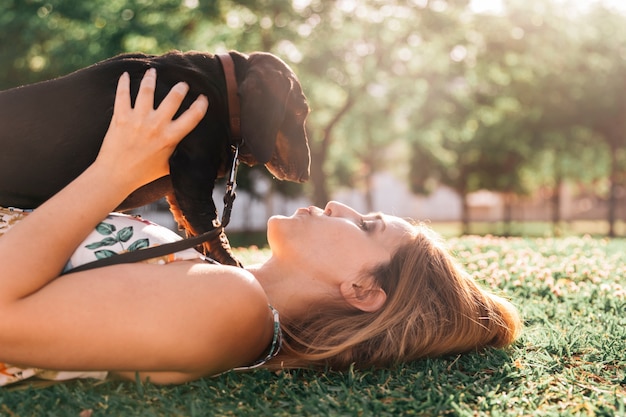 Hermosa mujer joven tumbado en la hierba verde besando a su perro en el parque