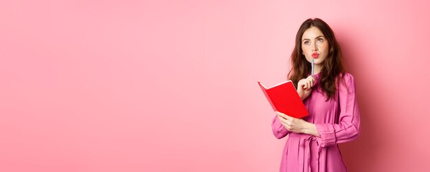 Hermosa mujer joven se ve pensativa escribiendo en un cuaderno con un planificador o un diario planificando su horario