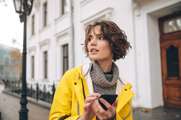 Hermosa mujer joven vestida con impermeable chateando