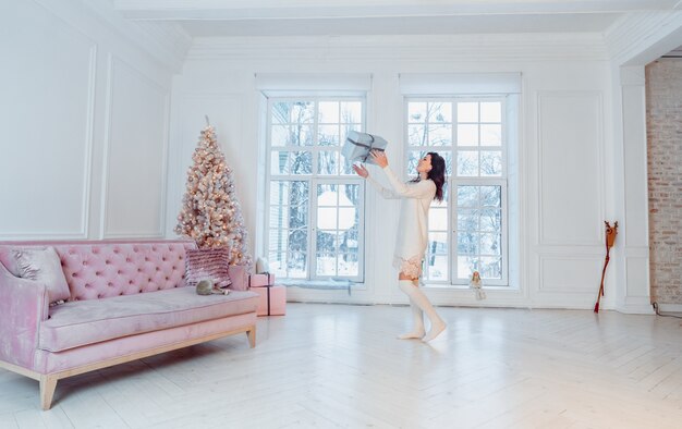 Hermosa mujer joven en vestido blanco posando con caja de regalo