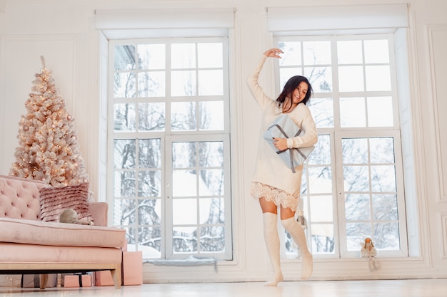 Hermosa mujer joven en vestido blanco posando con caja de regalo