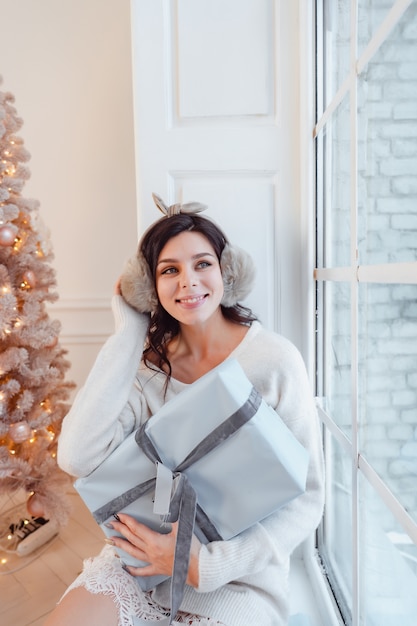 Hermosa mujer joven en vestido blanco posando con caja de regalo