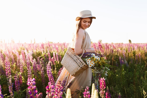 Hermosa mujer joven en vestido blanco y sombrero de paja caminando en campo de flores