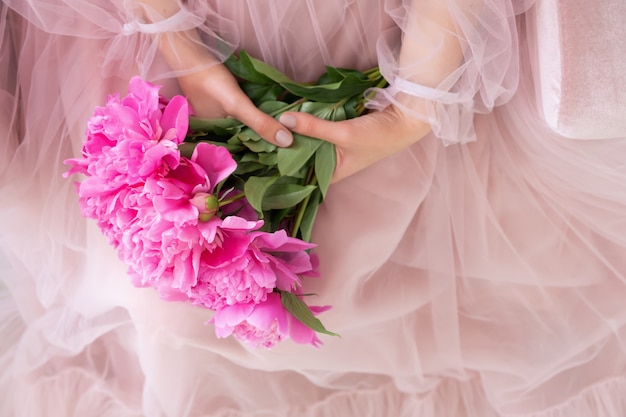 Hermosa mujer joven en vestido rosa con ramo de flores de peonía en sus manos