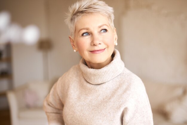 Hermosa mujer jubilada feliz vistiendo suéter acogedor y peinado corto