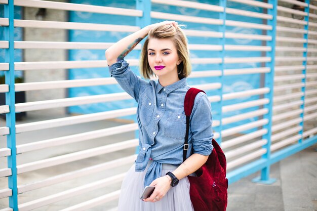 Hermosa mujer con labios de color rosa brillante sosteniendo su cabello con una mano y el teléfono inteligente con la otra mano