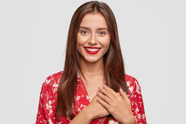 Hermosa mujer con lápiz labial rojo posando contra la pared blanca