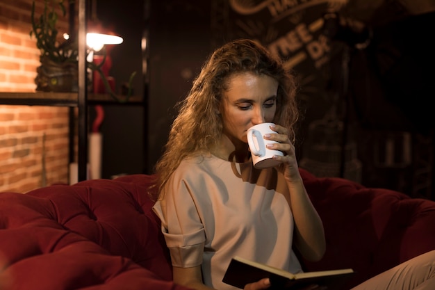 Hermosa mujer leyendo un libro en casa mientras bebe té