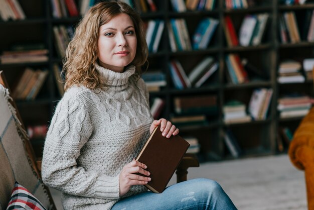 Hermosa mujer con libro cerca de librero