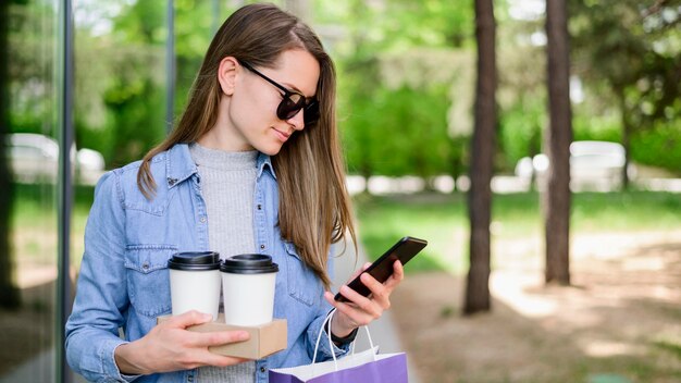 Hermosa mujer llevando café mientras revisa el teléfono