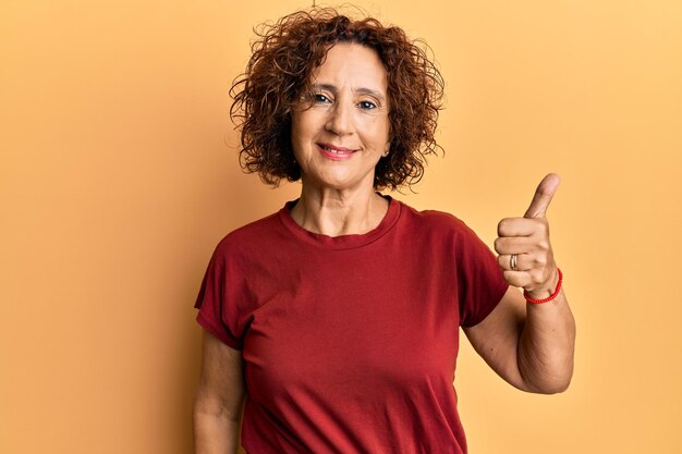 Hermosa mujer madura de mediana edad con ropa informal sonriendo feliz y positiva con el pulgar hacia arriba haciendo excelente y signo de aprobación