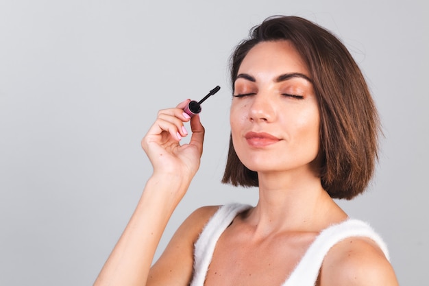 Hermosa mujer con maquillaje mantenga pincel de rímel negro sobre pared gris, concepto de belleza