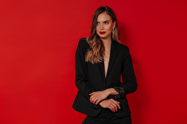 Hermosa mujer con maquillaje de noche vistiendo chaqueta negra posando sobre pared roja aislada