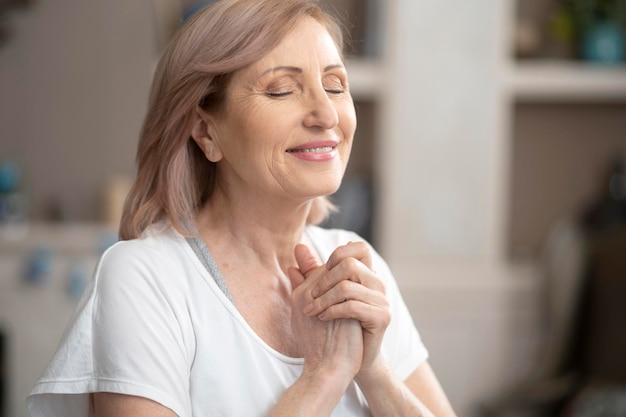 Hermosa mujer de más de 50 años disfruta del yoga. Está meditando ahuecando las palmas de sus manos frente a ella con los ojos cerrados. Sueña con un primer plano personal.