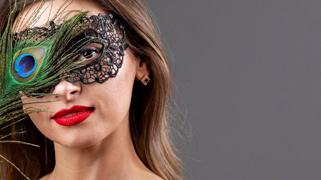 Hermosa mujer con máscara y pluma de pavo real
