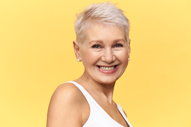 Hermosa mujer de mediana edad feliz con el pelo teñido corto mirando a la cámara con una amplia sonrisa alegre, riéndose de una broma divertida.