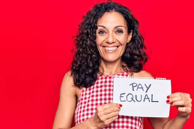 Foto gratuita hermosa mujer de mediana edad sosteniendo un papel de pago igual luciendo positivo y feliz de pie y sonriendo con una sonrisa segura mostrando los dientes