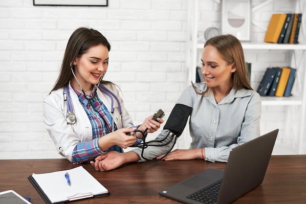 Foto gratuita hermosa mujer en un médico de familia mide la presión arterial con un tonómetro