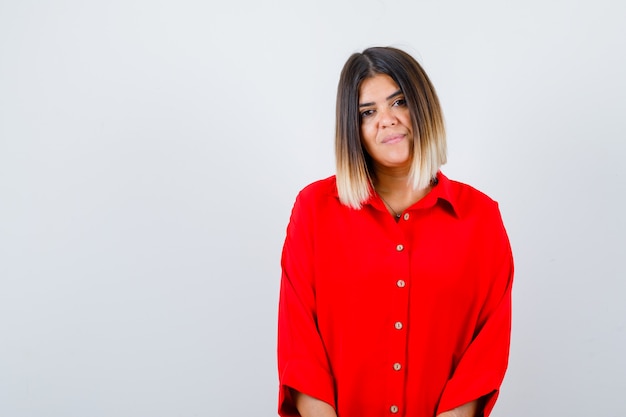 Hermosa mujer mirando a la cámara en blusa roja y luciendo delicada, vista frontal.