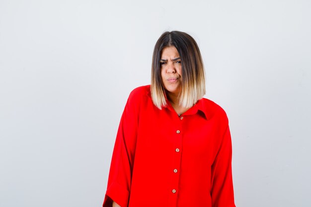 Hermosa mujer mirando a la cámara mientras fruncía el ceño en una blusa roja y miraba pensativa. vista frontal.