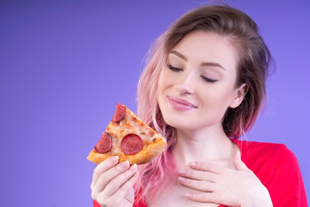 Hermosa mujer mirando una rebanada de pizza en su mano derecha