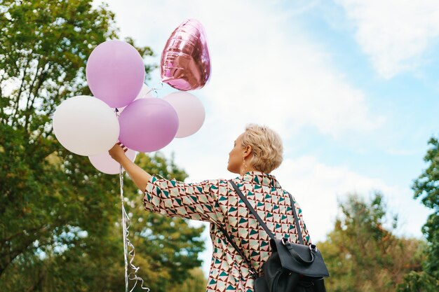 Hermosa mujer con mochila caminando feliz con globos rosas en el parque. Libertad y concepto de mujer sana.