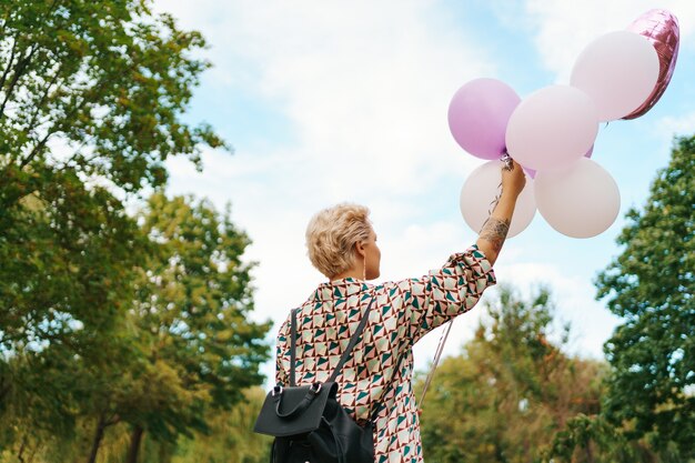 Hermosa mujer con mochila caminando feliz con globos rosas en el parque. Libertad y concepto de mujer sana.