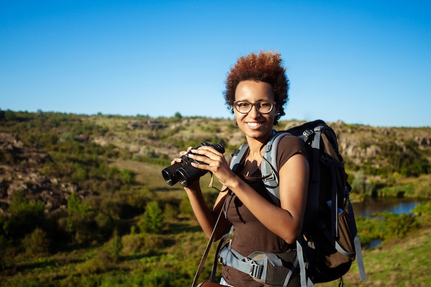 Hermosa mujer con mochila sonriendo, sosteniendo binoculares