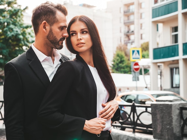 Foto gratuita hermosa mujer de moda y su novio elegante guapo en traje modelo morena sexy en vestido de noche negro pareja de moda posando en la calle en europa hombre brutal y su mujer al aire libre