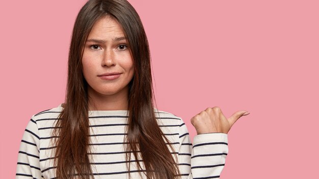 Hermosa mujer morena con cabello oscuro, piel pecosa, puntos con el pulgar, muestra espacio libre a un lado