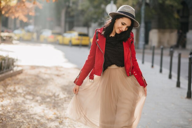 Hermosa mujer morena en falda larga beige caminando por el parque y mirando hacia abajo