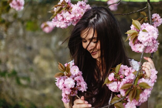 Hermosa mujer morena huele flores de color rosa en el floreciente árbol de sakura