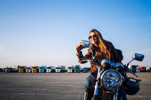 Hermosa mujer morena sentada en una motocicleta de estilo retro y mirándose en los espejos