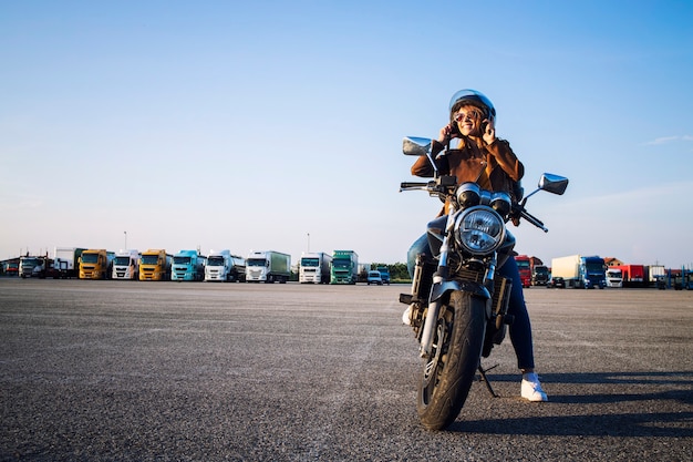 Hermosa mujer morena sexy en chaqueta de cuero sentada en una motocicleta de estilo retro preparándose para el paseo