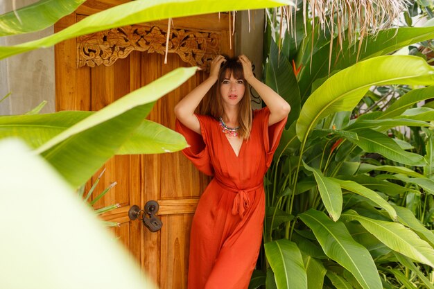 Hermosa mujer morena en traje de verano con estilo disfrutando de vacaciones en resort de lujo. Jardín exótico con plantas tropicales.