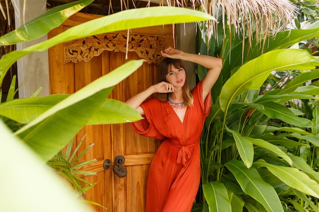 Hermosa mujer morena en traje de verano con estilo disfrutando de vacaciones en resort de lujo. Jardín exótico con plantas tropicales.