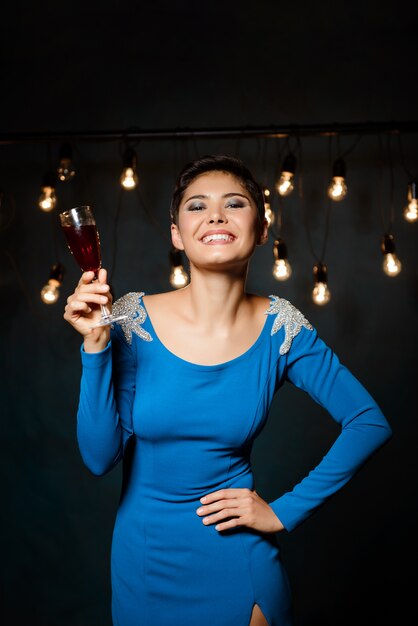 Hermosa mujer morena en vestido de noche sonriendo, sosteniendo una copa de vino