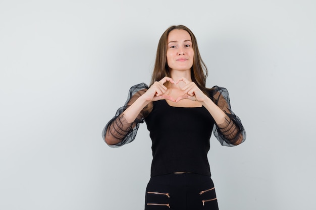 Hermosa mujer mostrando gesto de paz en blusa negra y aspecto adorable. vista frontal.