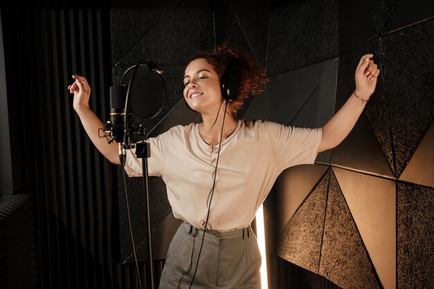 Hermosa mujer músico en auriculares bailando y cantando sensualmente en estudio de grabación de sonido