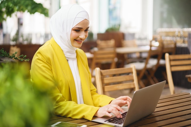 Hermosa mujer musulmana sonriente con portátil en el café