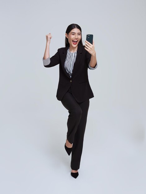 Hermosa mujer de negocios asiática usando teléfono móvil y feliz celebración sobre fondo blanco de estudio