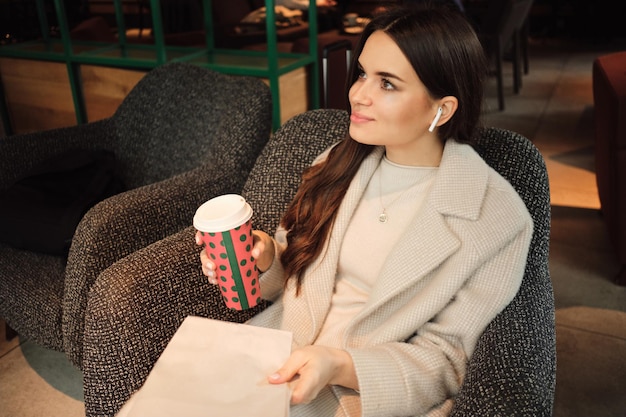 Hermosa mujer de negocios con estilo en auriculares inalámbricos descansando en un café con café y periódico