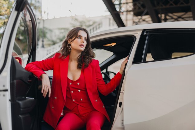 Hermosa mujer de negocios rica sexy en traje rojo posando en coche blanco