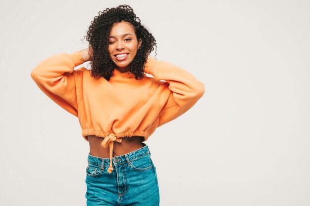 Hermosa mujer negra con peinado afro rizos. Modelo sonriente en sudadera con capucha naranja y ropa de jeans de moda